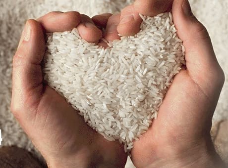 Hands picking up raw white rice in the shape of a heart