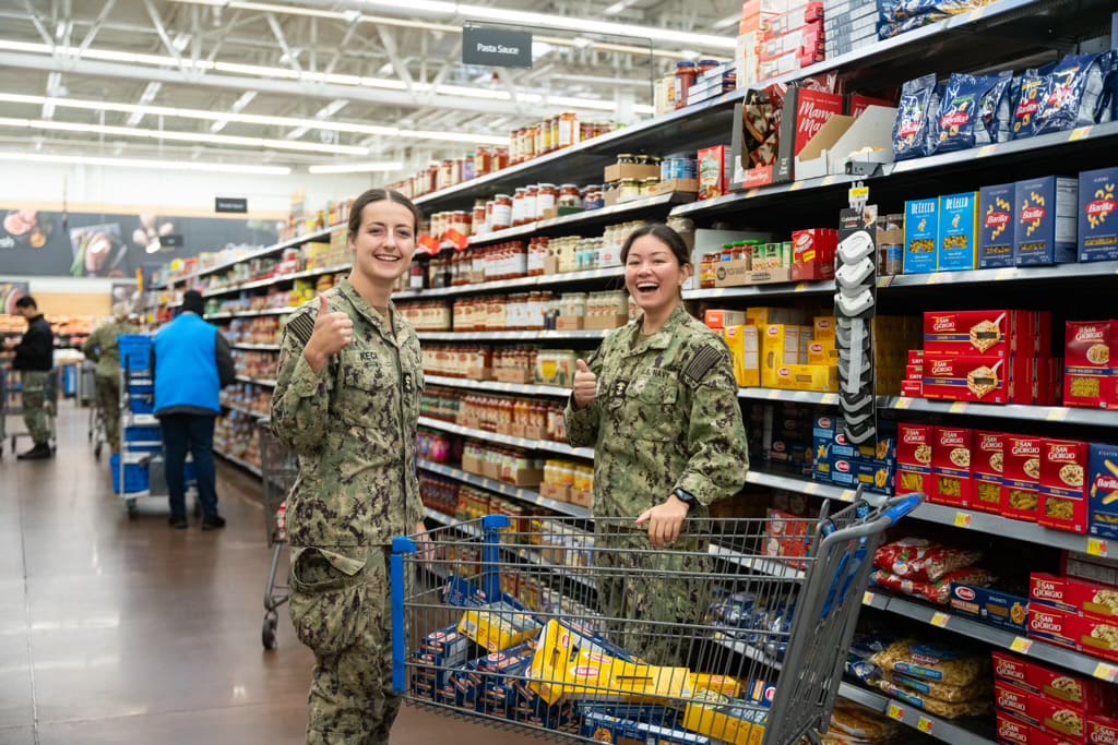 Military women in grocery store buying food items and giving thumbs up to the camera